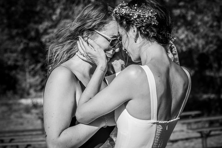 Photographie de mariage de Tiphaine et Guy en noir et blanc. Moment de complicité entre soeur, sa soeur pleure pour le mariage de tiphaine et elle vient tendrement lui mettre ses mains sur la partie basse de son visage pour venir la rassurer et la câliner. Photographie prise par un photographe de mariage professionnel