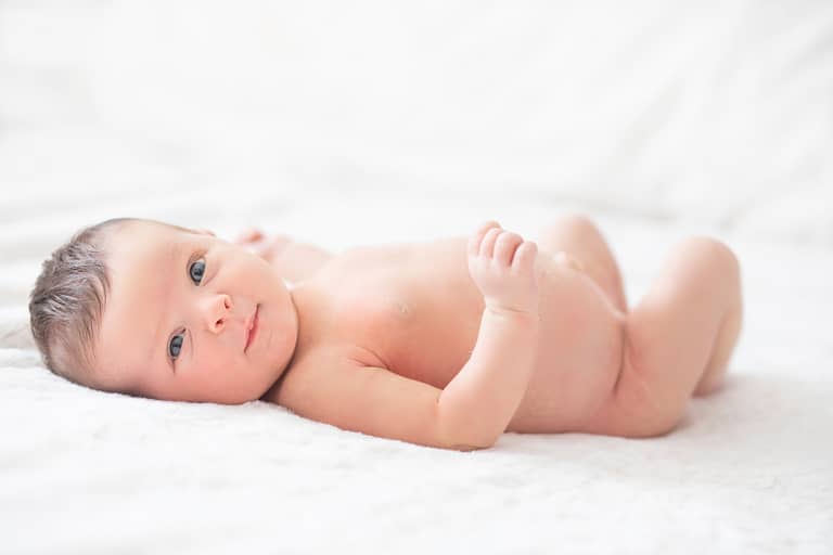 photo bébé nu sur un lit avec un drap blanc, prise par un photographe professionnel de naissance, nouveau-né et bébé